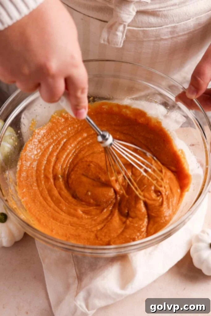A glass bowl holds the whisked wet ingredients for pumpkin cake, showcasing the smooth, creamy consistency before dry ingredients are added.