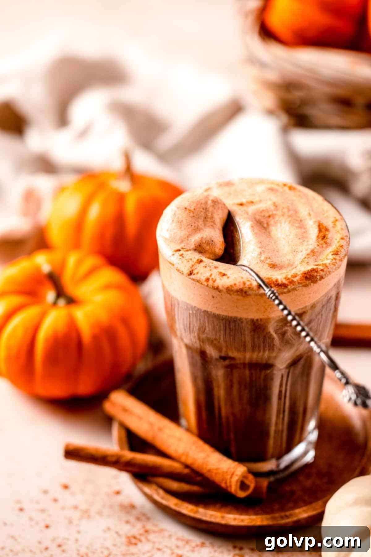 Iced coffee topped with a thick layer of creamy pumpkin cold foam, with a spoon and miniature pumpkins decoratively arranged around the glass, evoking a cozy fall atmosphere.