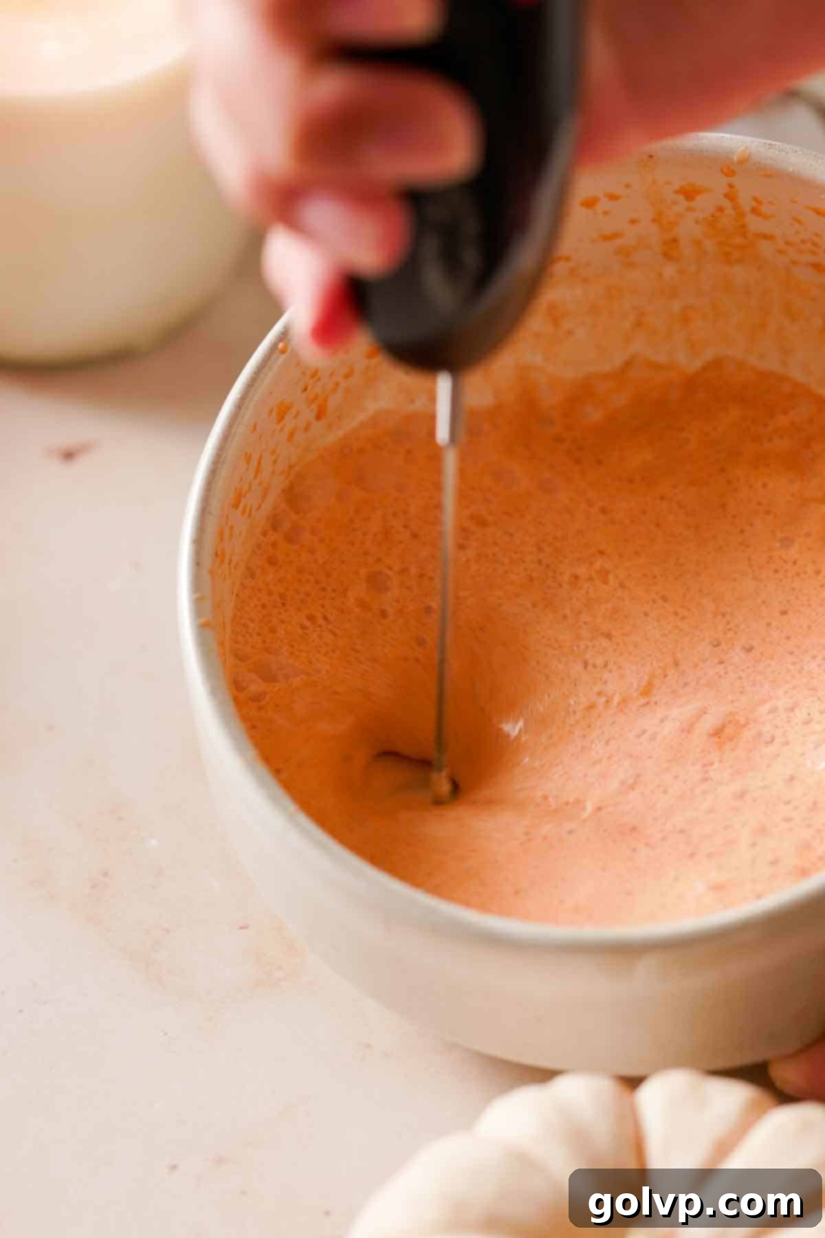 Whipping a mixture of pumpkin, cream, and spices in a glass jar until it becomes light and frothy, demonstrating the initial step of making cold foam.