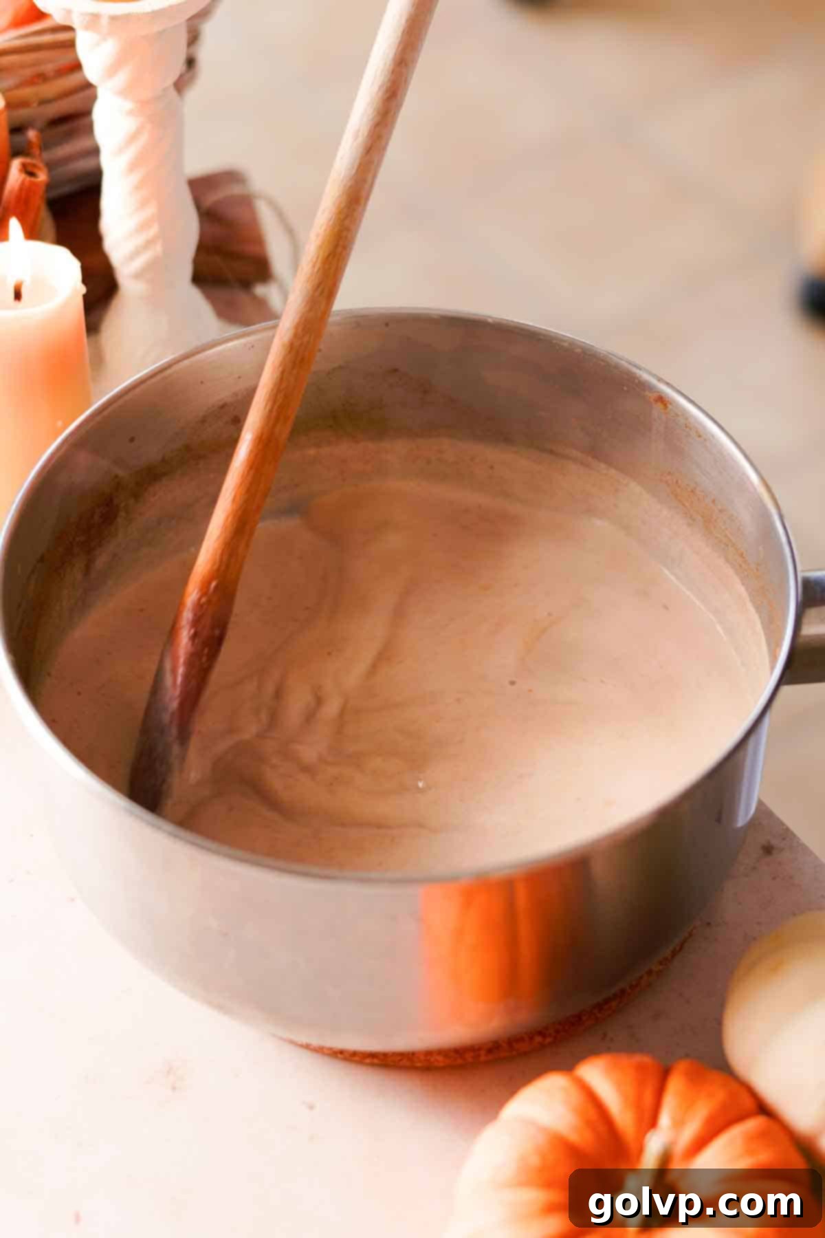 Stirring milk into the spiced pumpkin mixture in a saucepan with a wooden spoon