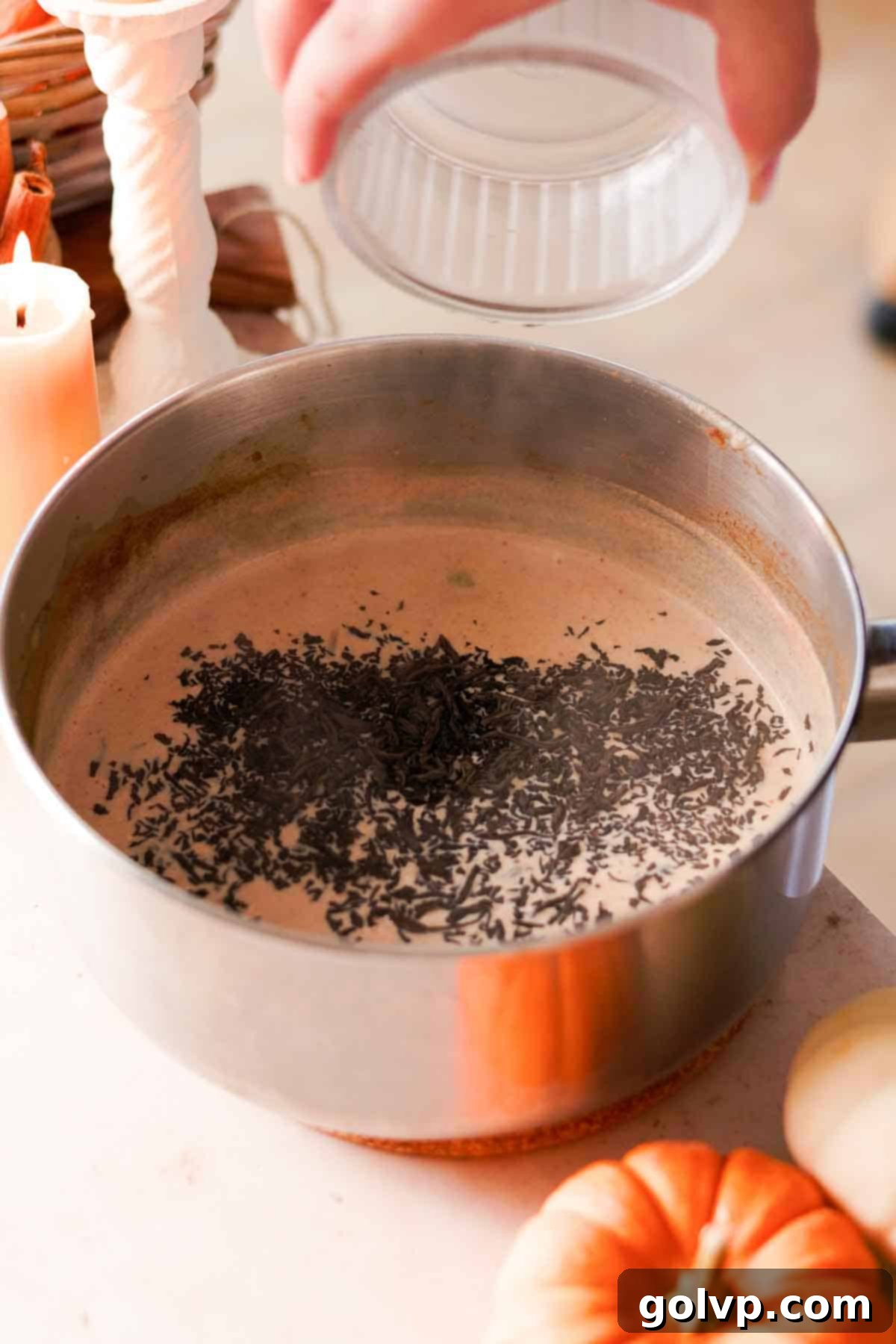 Adding loose leaf black tea leaves to hot chai in a pot for steeping