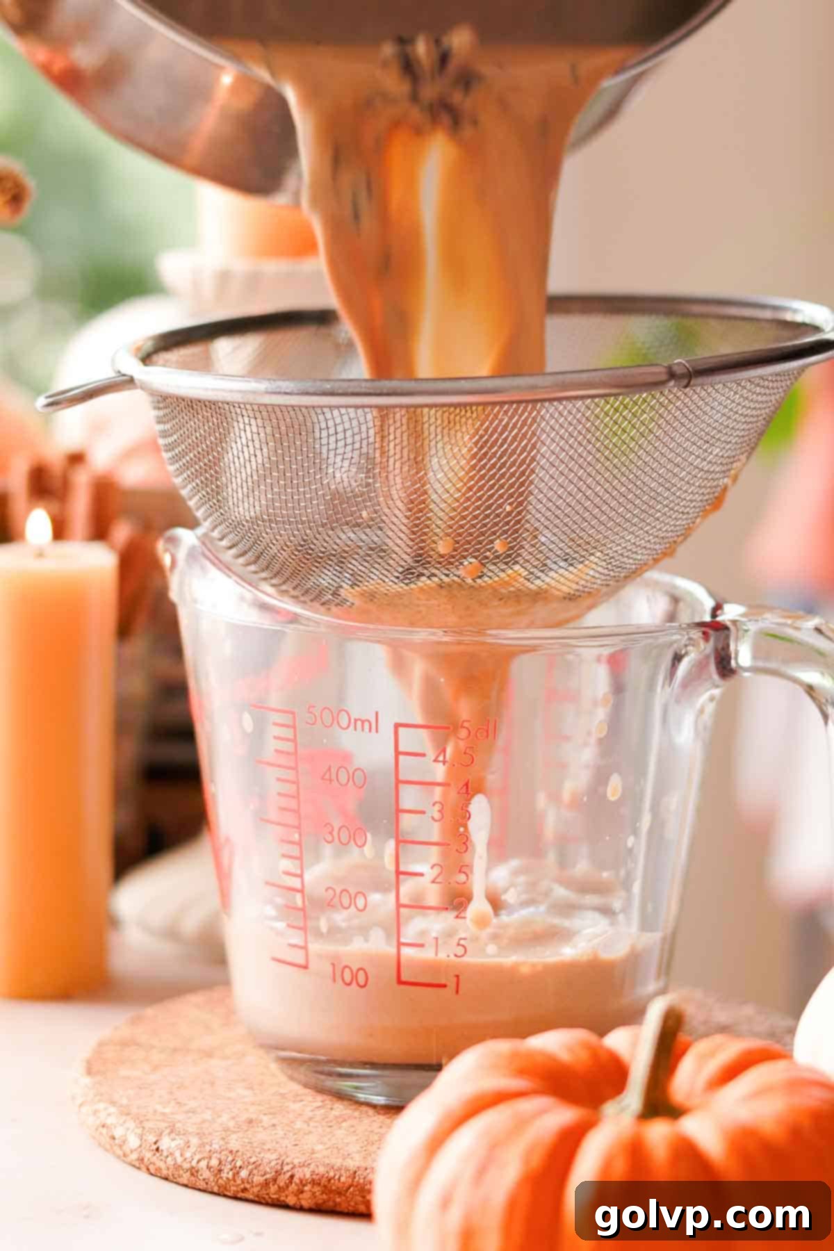 Straining pumpkin spice chai latte through a metal sieve into a glass measuring cup