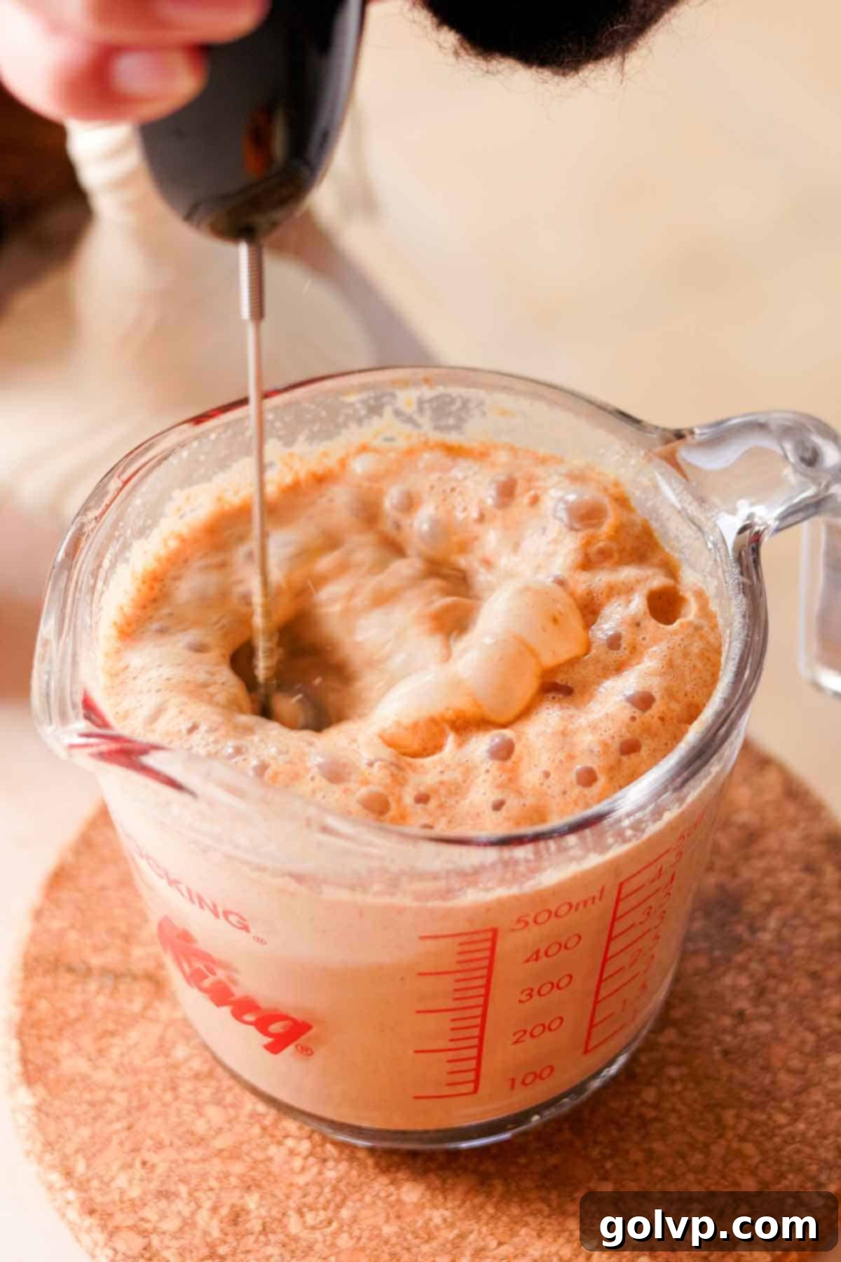Frothing pumpkin chai latte in a glass measuring cup with an electric whisk frother