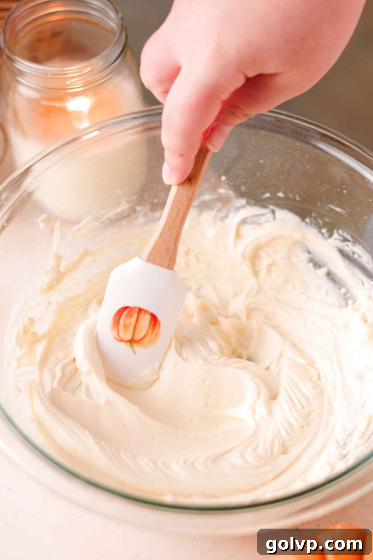 A spatula running through a bowl of creamy, whipped cream cheese and powdered sugar mixture, showing its smooth texture.