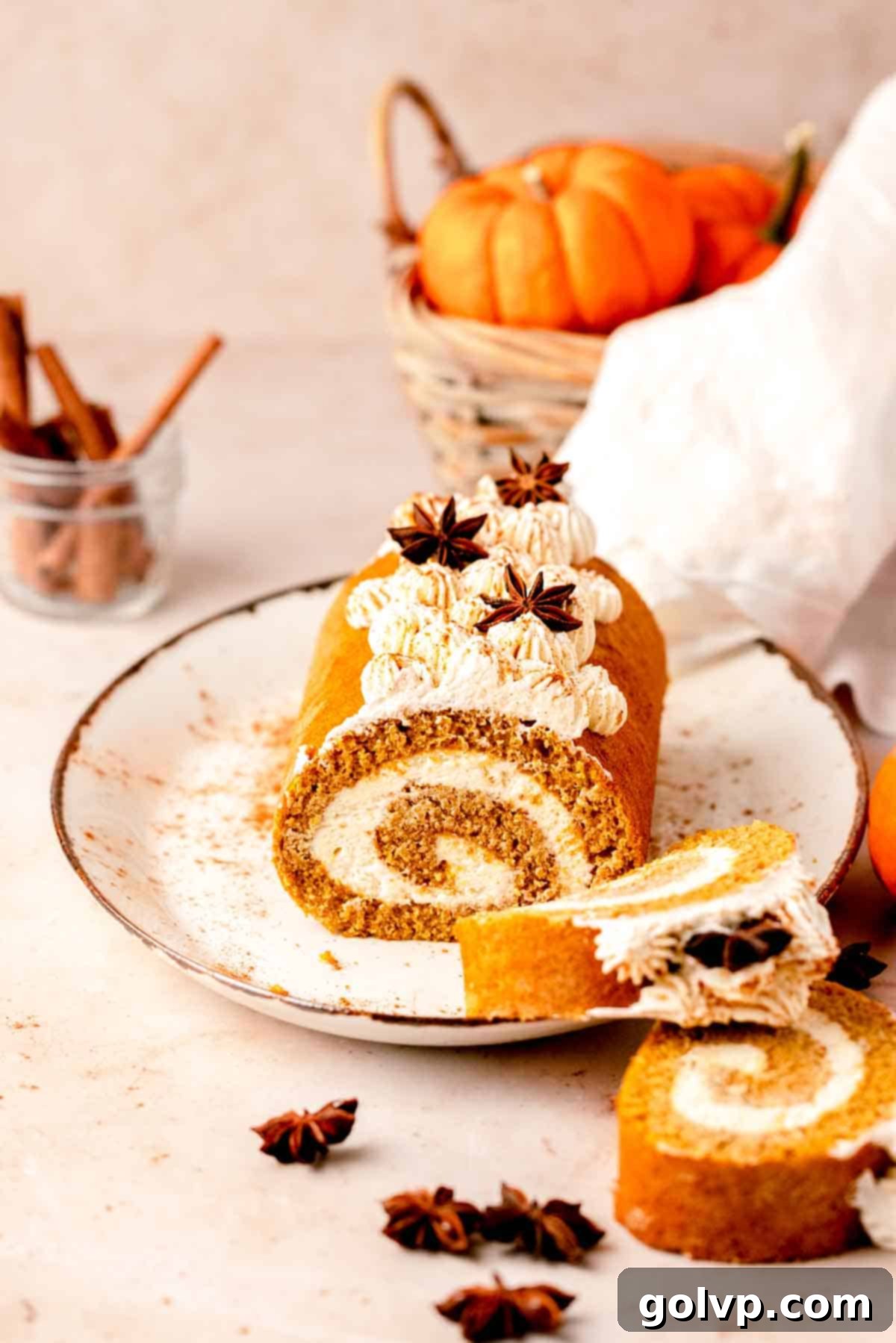 A beautifully decorated pumpkin roll with cheesecake filling and piped whipped cream on a plate, surrounded by mini decorative pumpkins, ready for a fall celebration.