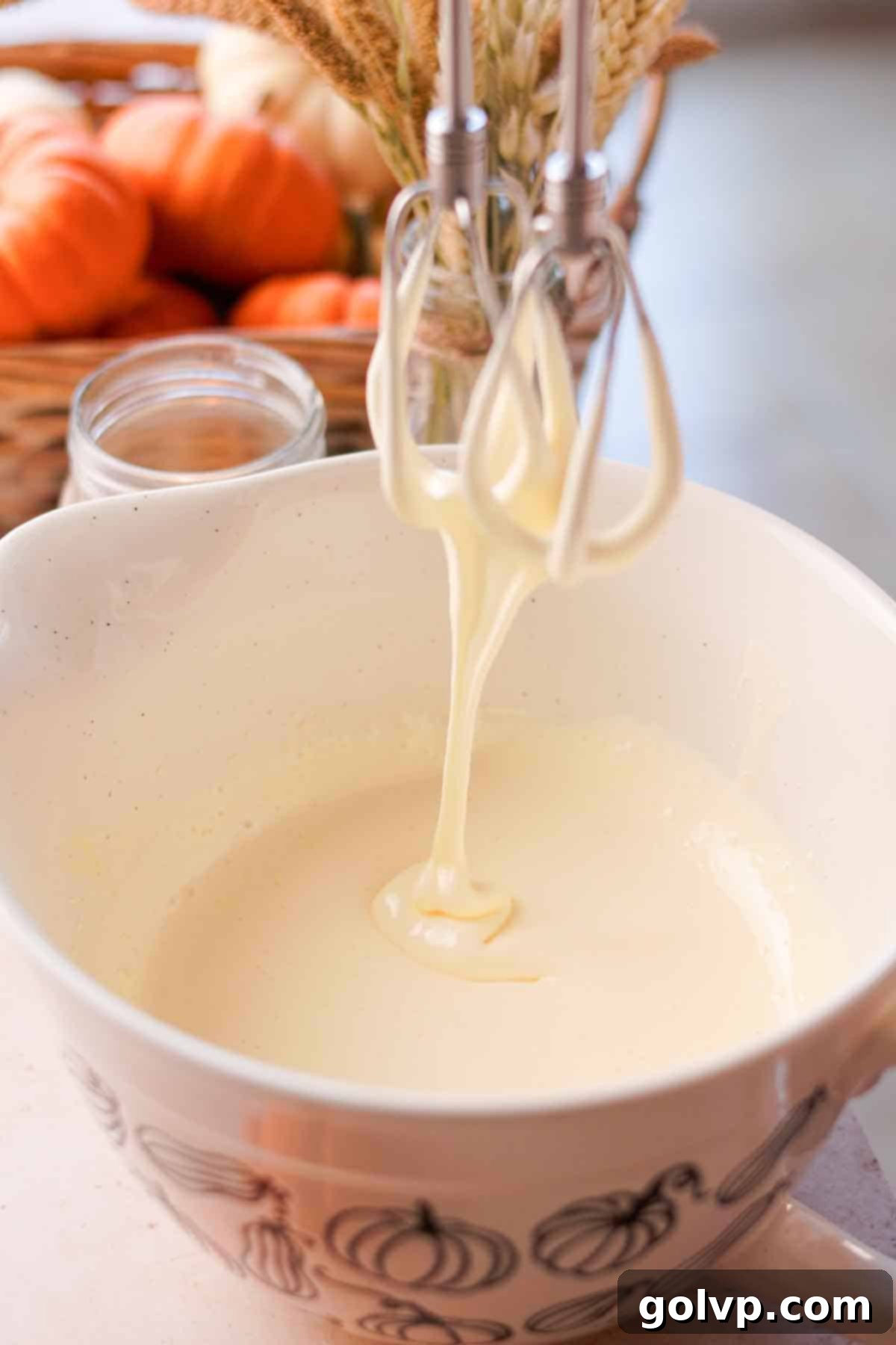 Close-up of whipped eggs and sugar forming thick ribbons as they fall from electric mixer beaters, indicating perfect consistency.