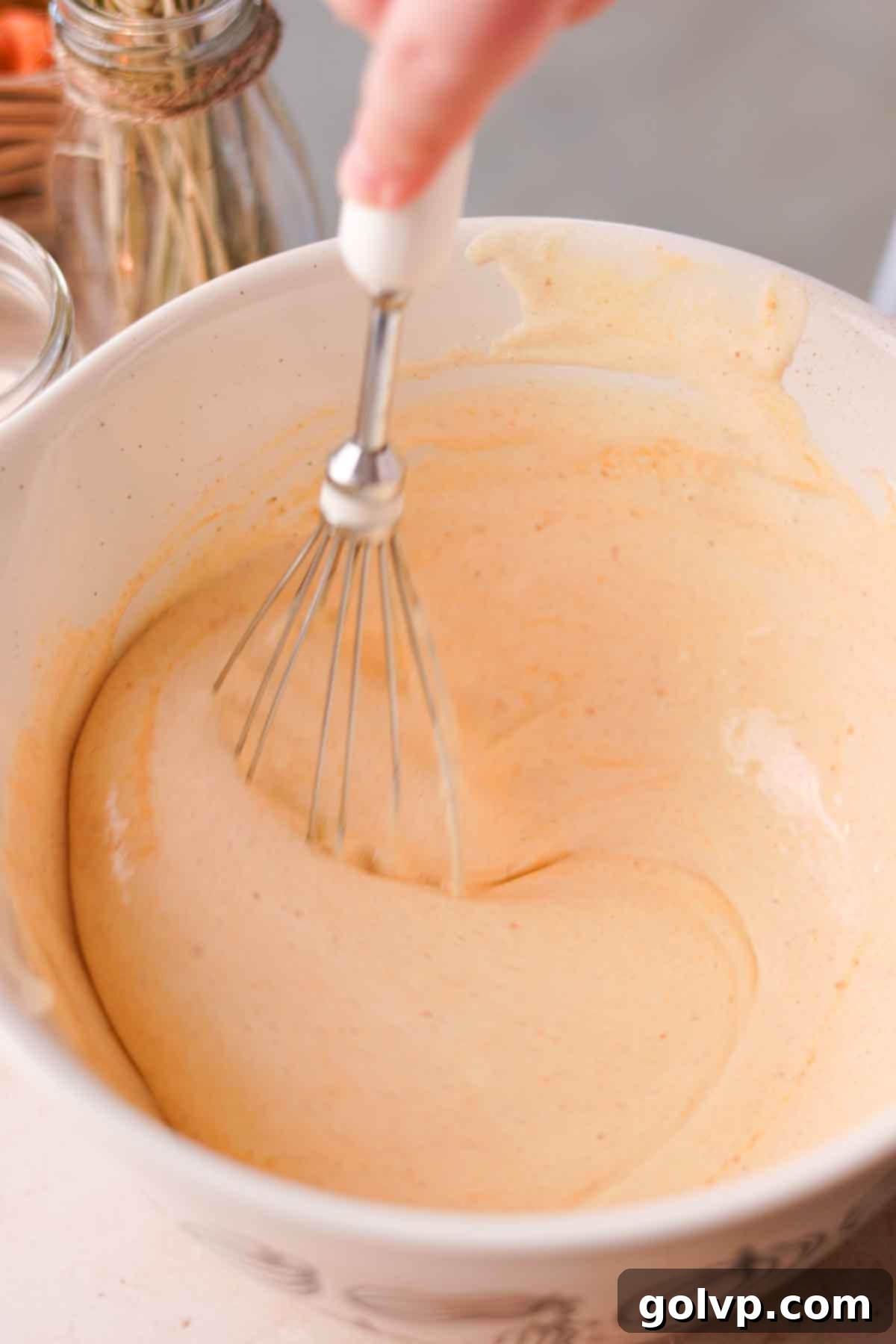 A wire whisk gently folding pumpkin puree into the light and airy beaten egg and sugar mixture in a glass bowl.