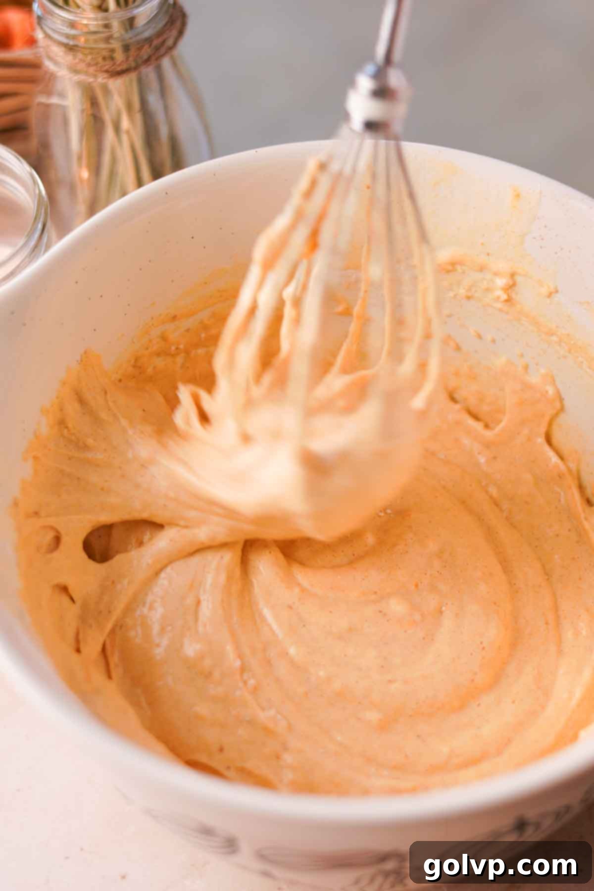 Pumpkin roll cake batter, light orange in color, being gently folded with a whisk in a large mixing bowl.