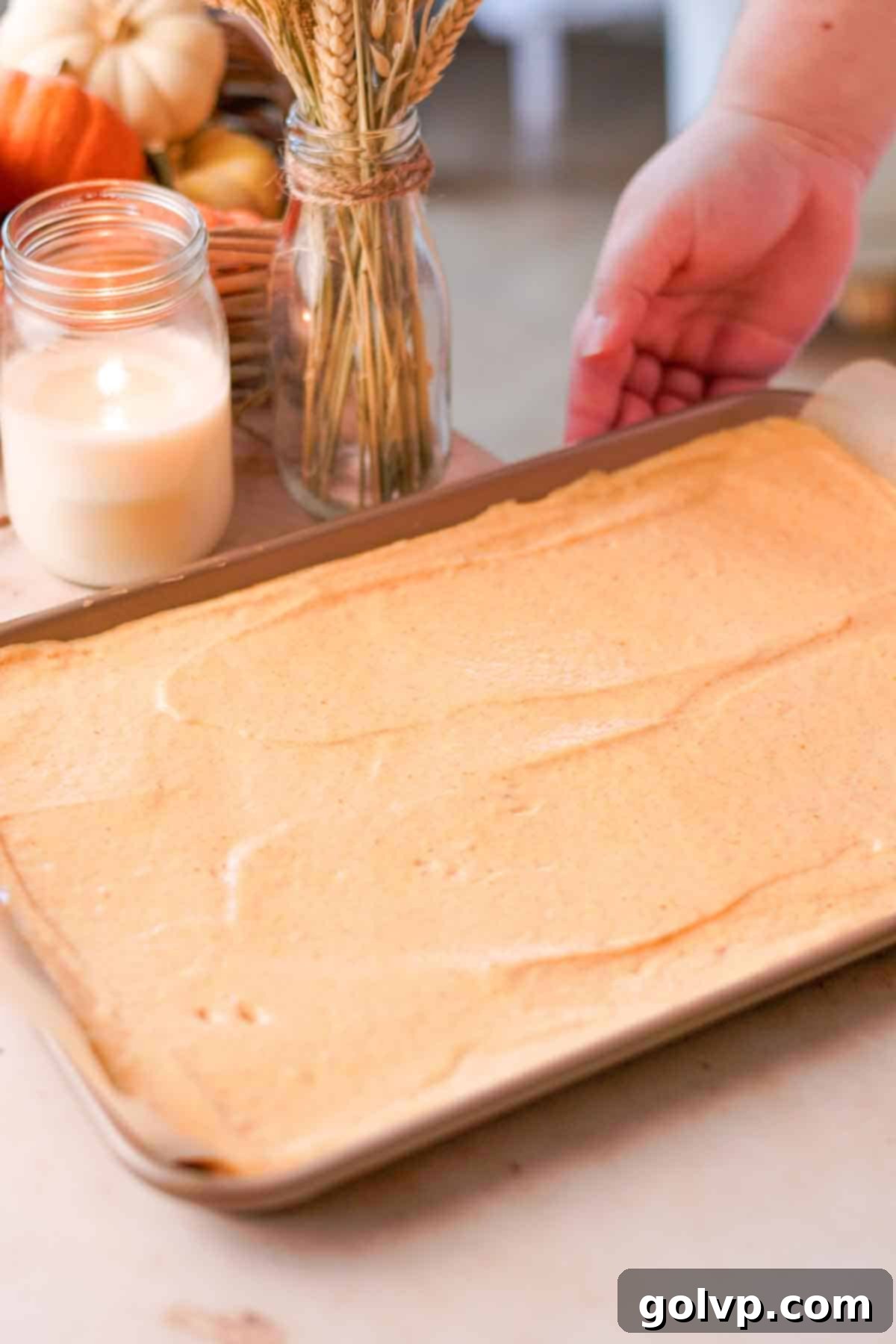 Smooth pumpkin cake batter evenly spread in a parchment-lined baking pan, ready to be baked.