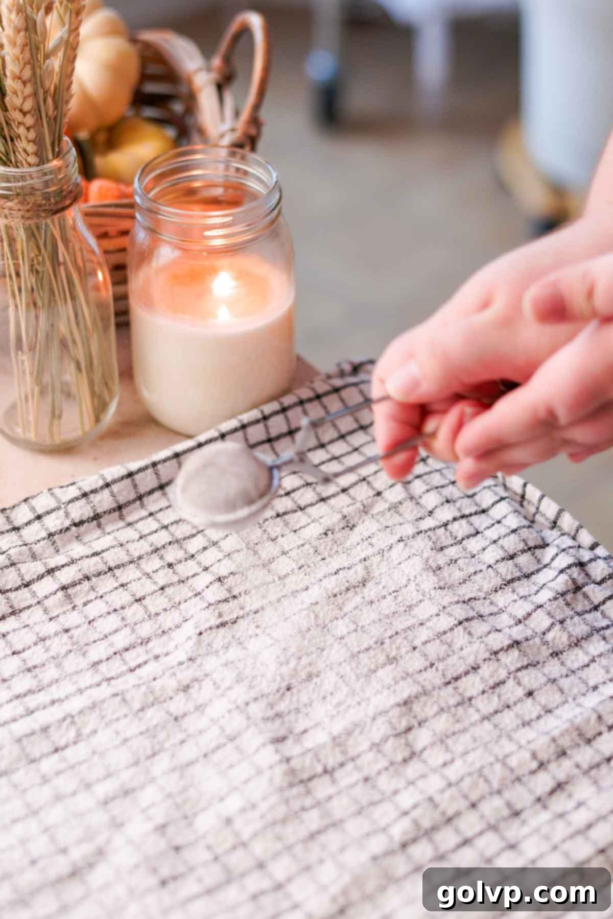 A clean, white kitchen towel lightly dusted with powdered sugar, laid out flat in preparation for rolling the pumpkin swiss roll.
