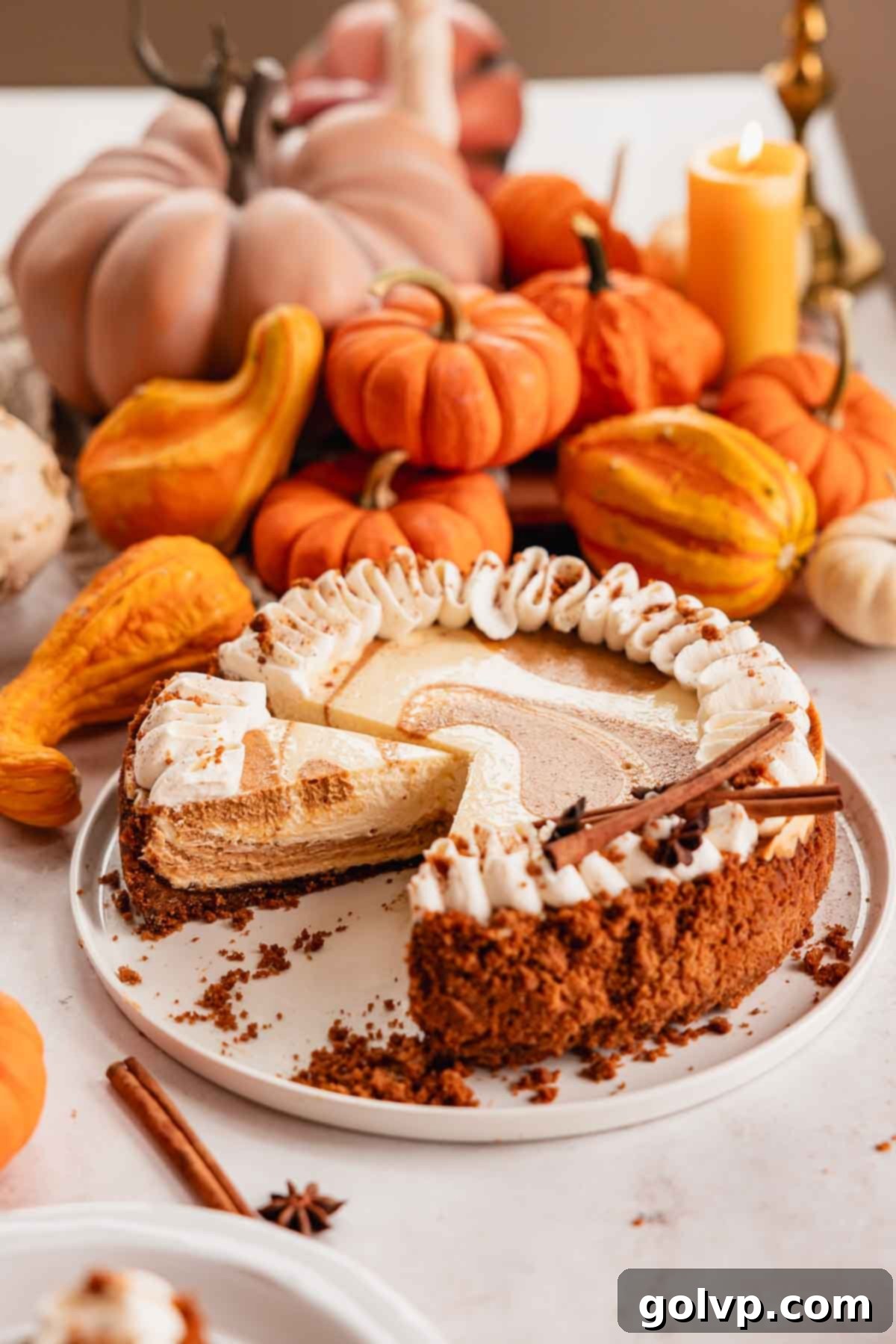 sliced pumpkin pie cheesecake on cake plate with whipped cream