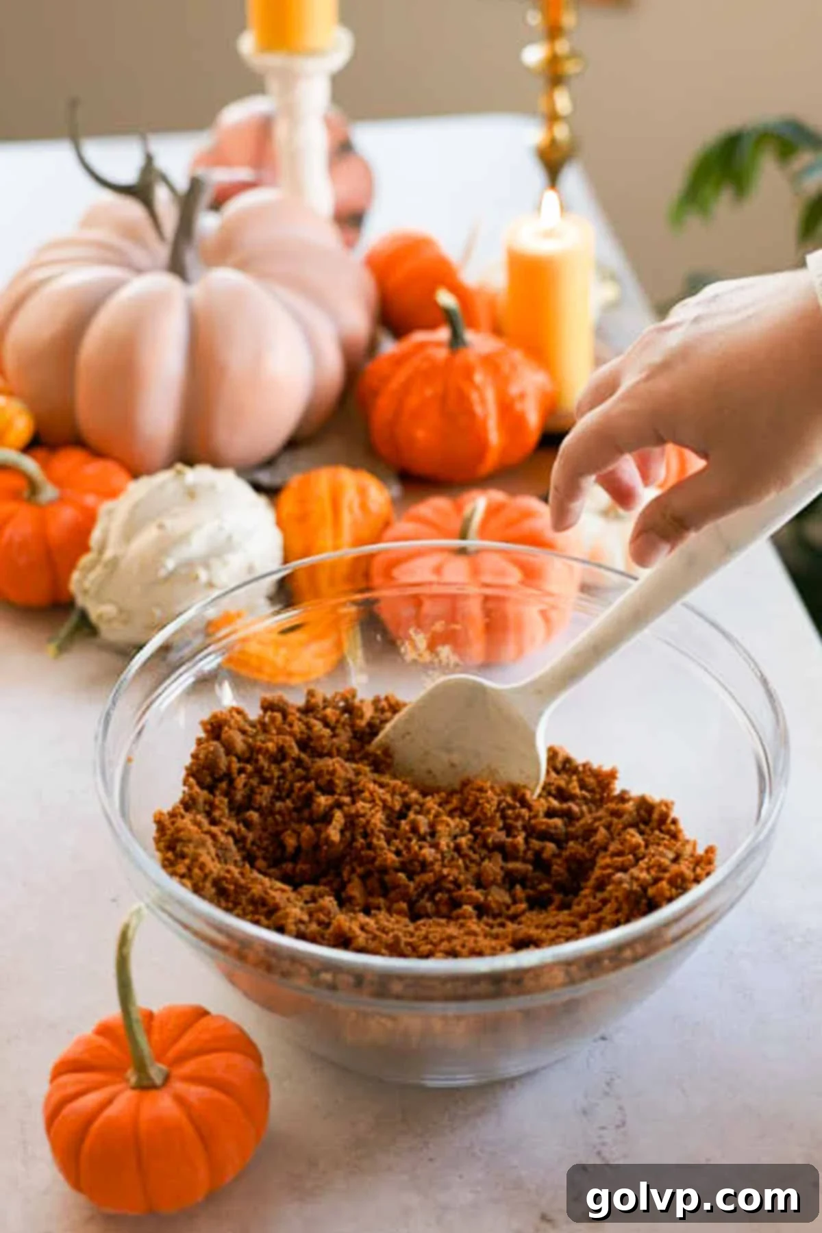 mixing biscoff cheesecake crust in a large glass bowl with a silicone spatula