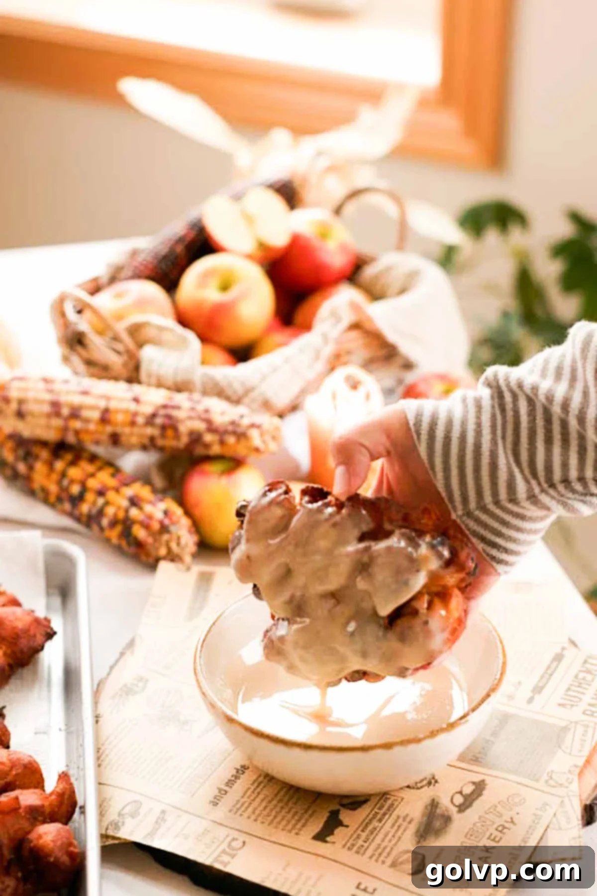 dipping apple fritters into a bowl with glaze