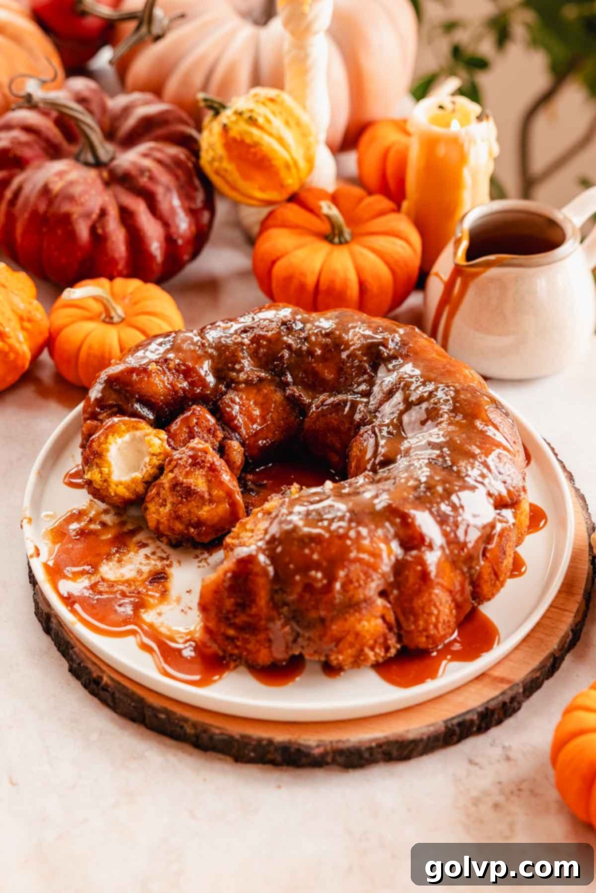 A freshly baked pumpkin monkey bread, generously covered in caramel sauce, presented on a large serving plate.