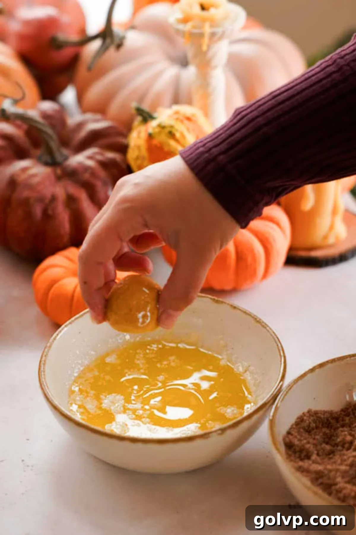 Pumpkin monkey bread balls being dipped in a bowl of melted butter before coating.