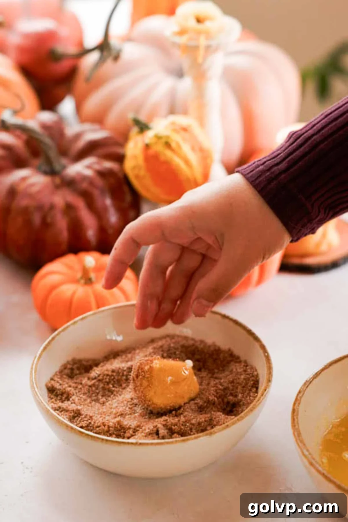 Coated pumpkin monkey bread dough balls being rolled in a bowl of pumpkin spice and sugar mixture.