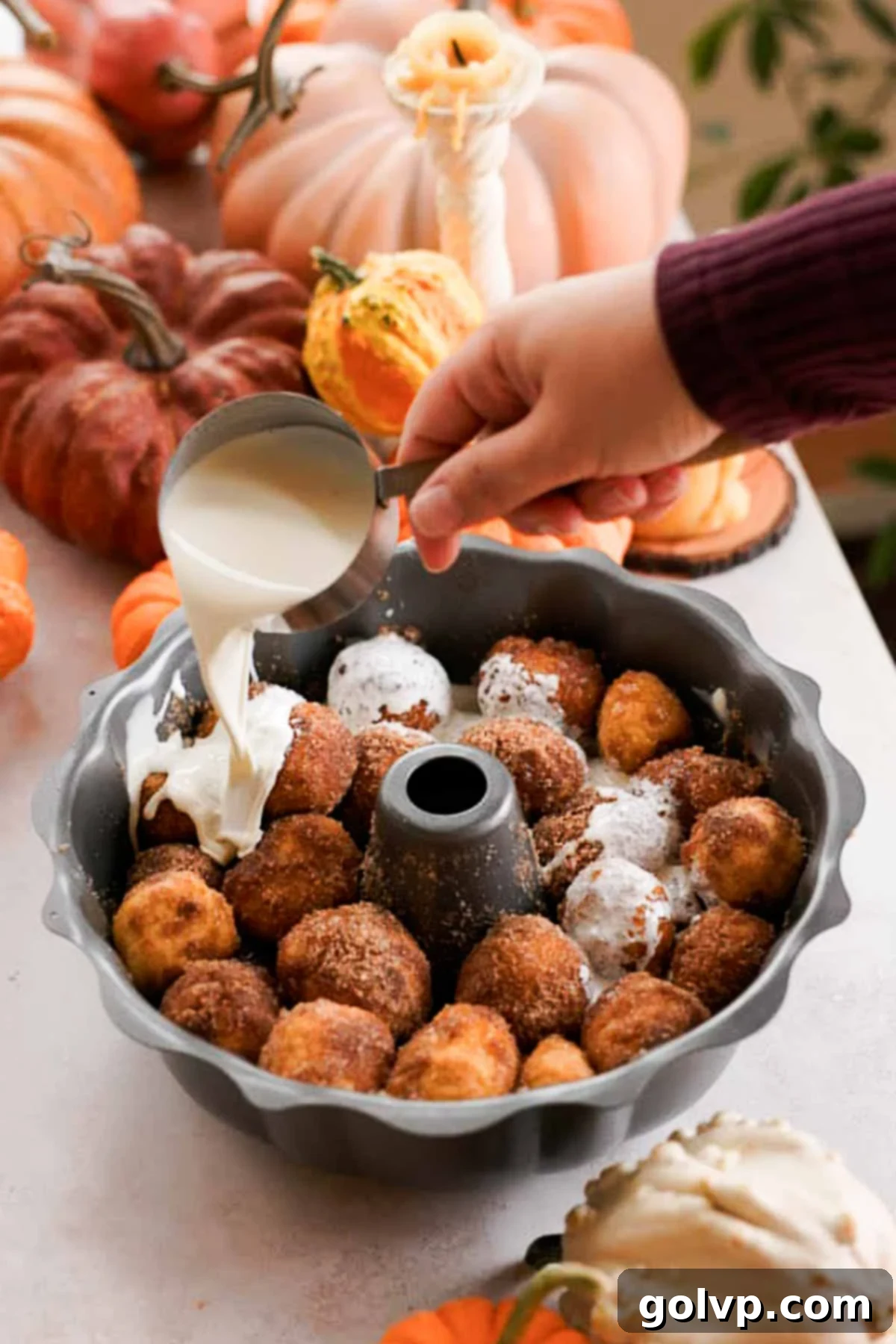 Heavy cream being poured evenly over pumpkin monkey bread dough in a bundt pan just before baking.