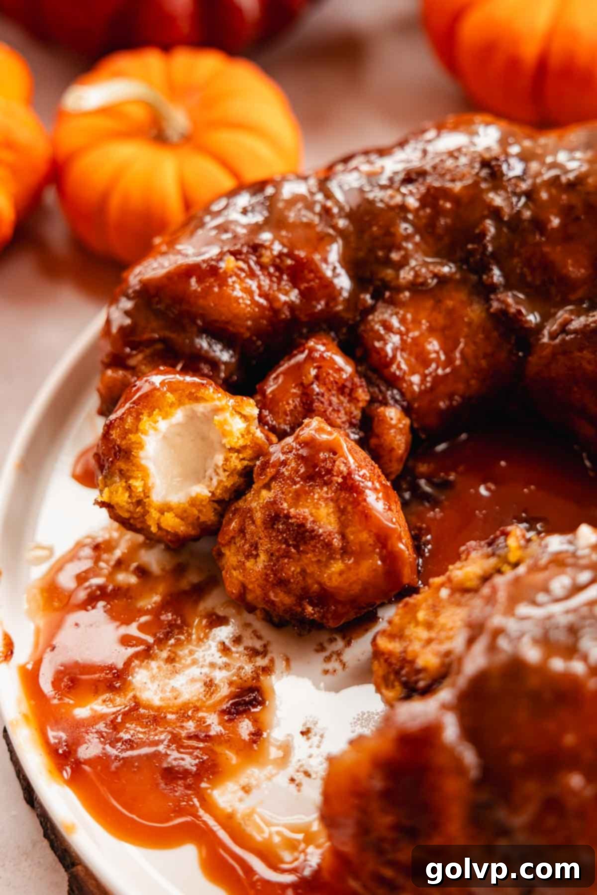 A close-up of a pumpkin monkey bread piece, torn open to reveal the molten cream cheese filling inside.