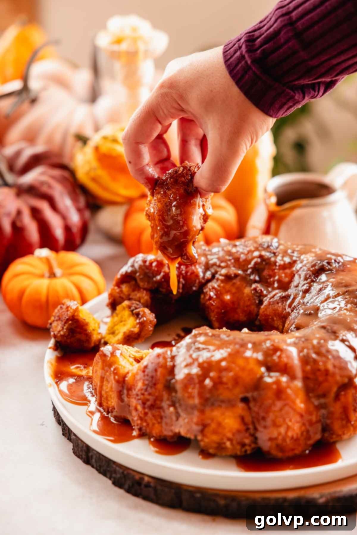 A hand pulling a single piece of caramel-coated pumpkin monkey bread, revealing its soft, gooey texture.