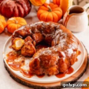 Pumpkin Monkey Bread with Cream Cheese Filling, glistening with caramel sauce on a large white plate, ready to be served.
