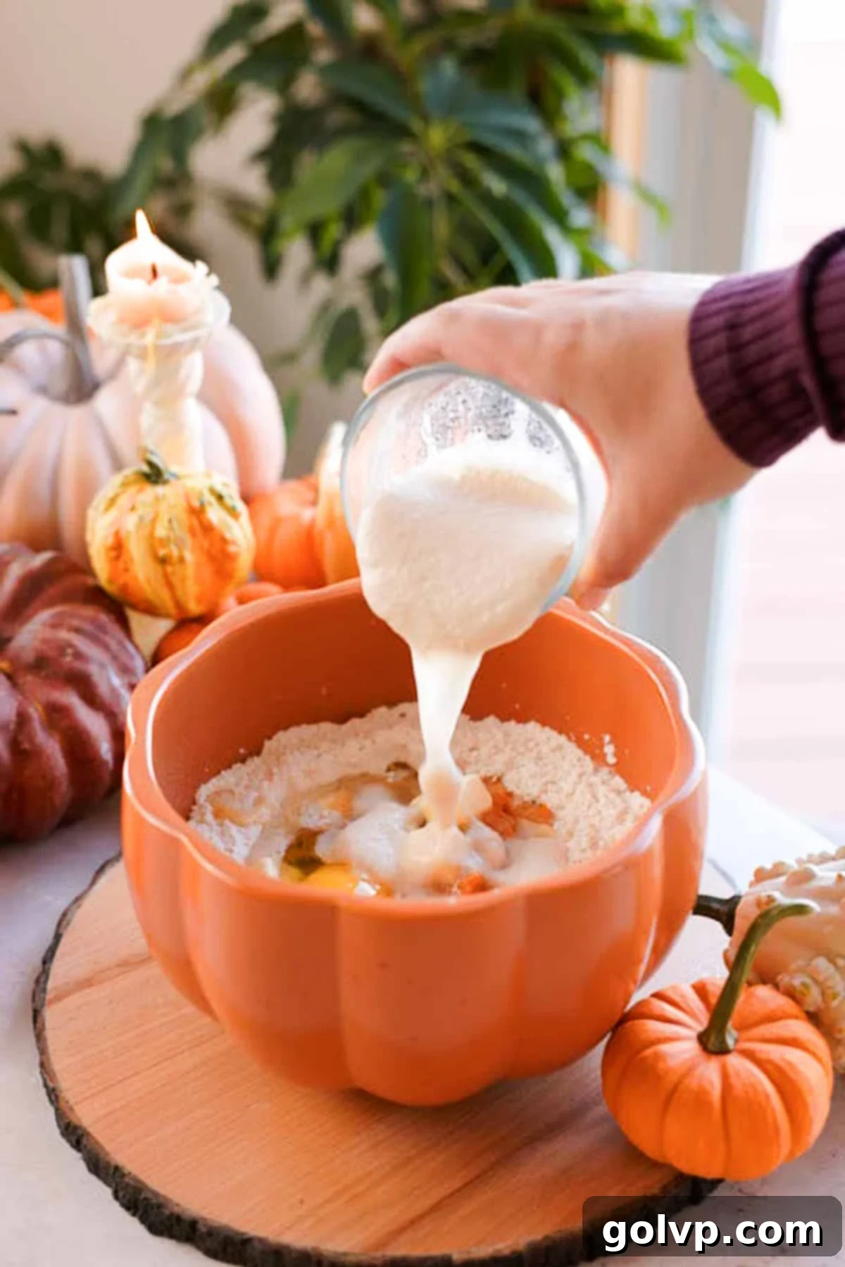 A stream of dissolved yeast mixture being poured into a large bowl containing pumpkin monkey bread dough ingredients.