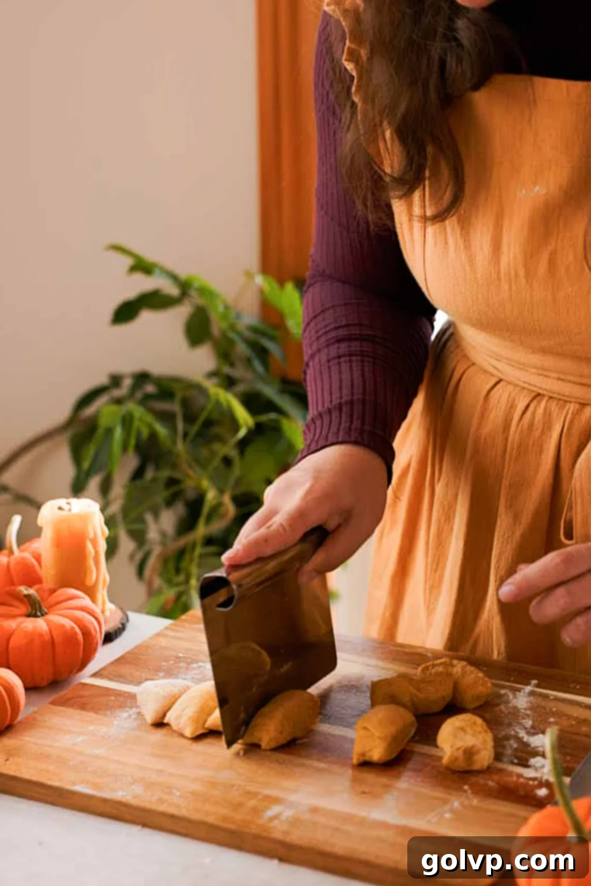 Pumpkin dough being cut into small, even pieces on a lightly floured surface.
